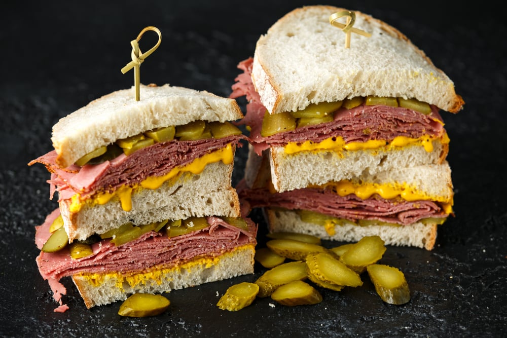 A towering, traditional New York pastrami on rye sandwich with spicy brown mustard and pickles, a staple of the best Jewish delis in NYC.